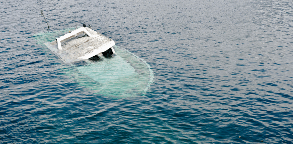 A partially sunken boat tilts in calm water, with its hull submerged and only the roof visible