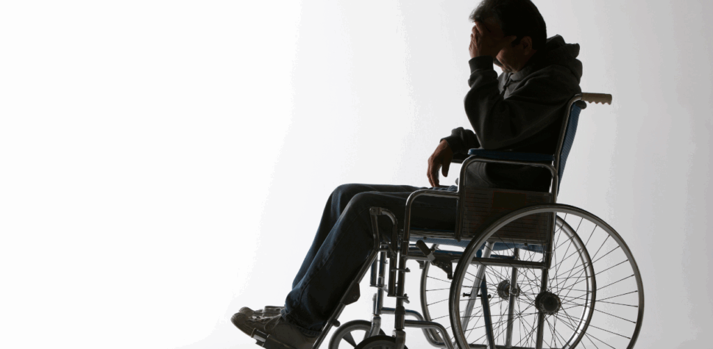 Man sits in a wheelchair with his head in his hand, silhouetted against a white background, conveying emotional distress or life after a disabling injury