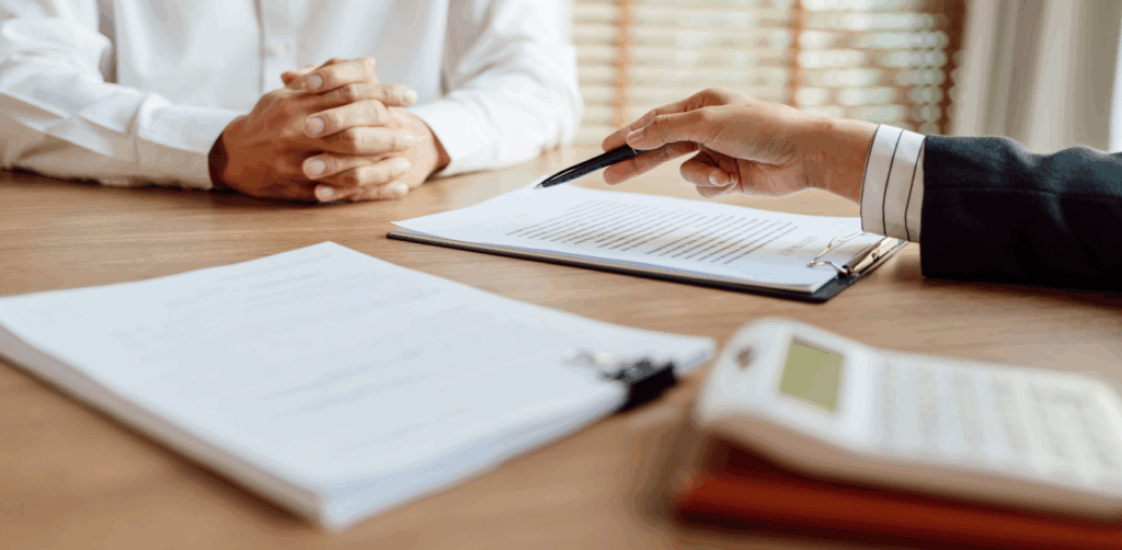 Professional in business attire points to a document on a clipboard during a consultation, while the other person listens with folded hands, possibly reviewing a rideshare accident claim