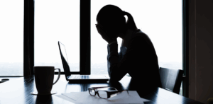 Silhouette of a woman sitting at a desk with her head in her hands in front of a laptop, illustrating emotional distress or the mental toll of dealing with a personal injury case