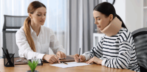Woman wearing a neck brace signs legal documents with the guidance of a professional, suggesting a personal injury consultation or insurance claim process