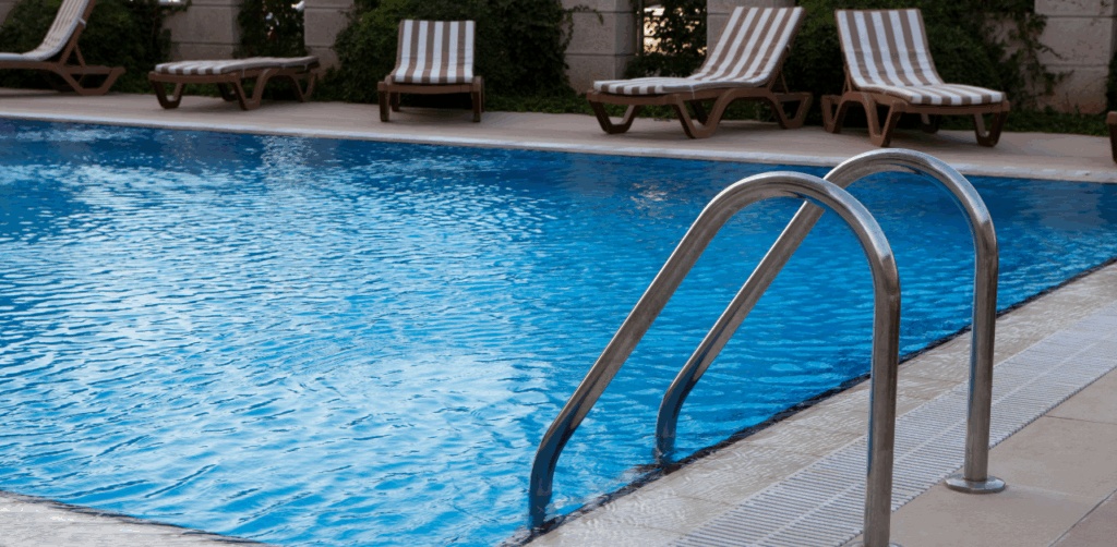 Clear outdoor swimming pool with metal handrails and striped lounge chairs nearby