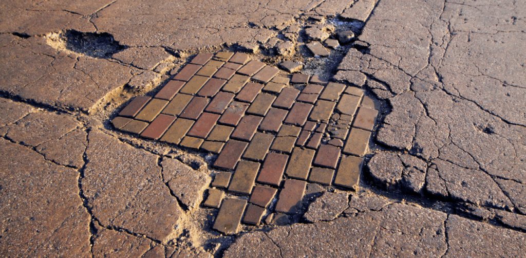 Damaged asphalt reveals old brick road beneath with cracks and potholes