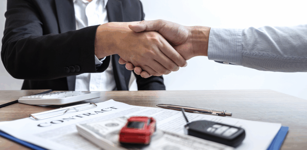 Two people shake hands over a car contract, symbolizing a successful auto sale or lease deal