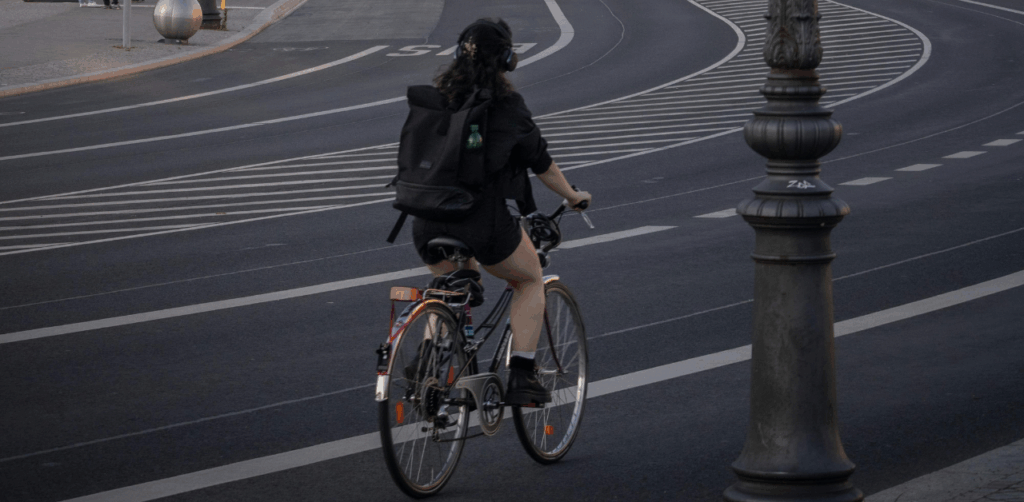 Woman rides bicycle alone in marked city bike lane with backpack