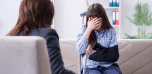Injured woman with arm in sling and crutch, covering her face while speaking with a professional