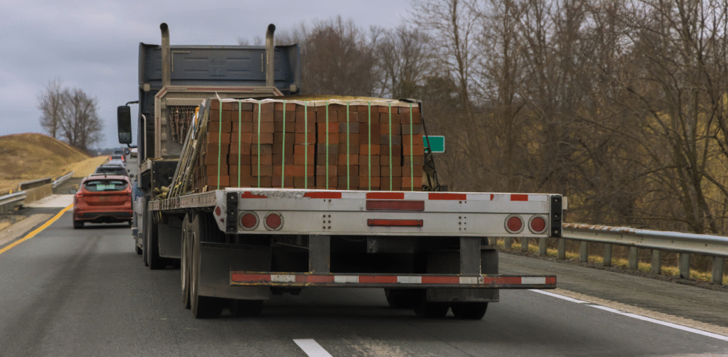Flatbed truck carrying stacked bricks on highway, highlighting commercial vehicle traffic and road safety