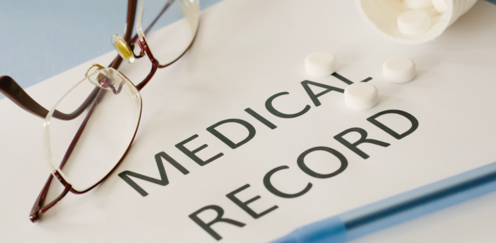Medical record folder with eyeglasses and scattered white pills beside an open prescription bottle