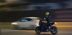 Motorcyclist riding at night beside a moving car, captured with motion blur on a city street