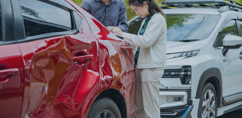 Damaged red car inspected after a crash as a person records details beside the vehicle