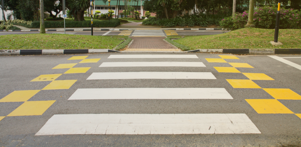 Marked pedestrian crosswalk with white stripes and yellow checkerboard safety markings across a road